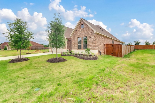 view of side of home featuring a yard, brick siding, concrete driveway, and fence