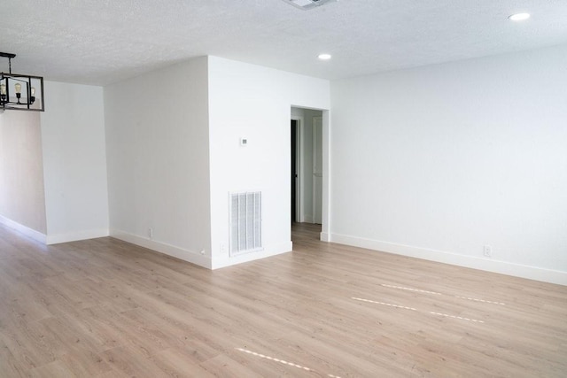 empty room with a textured ceiling, light hardwood / wood-style flooring, and a notable chandelier