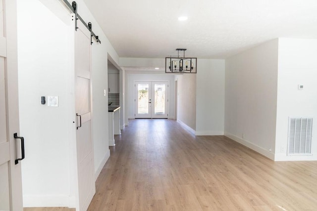 interior space featuring a barn door, light hardwood / wood-style flooring, an inviting chandelier, and french doors