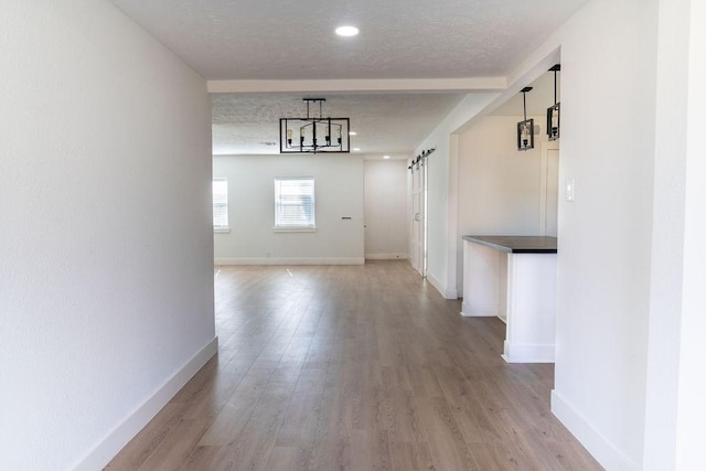 hall with an inviting chandelier, a barn door, light hardwood / wood-style flooring, and a textured ceiling