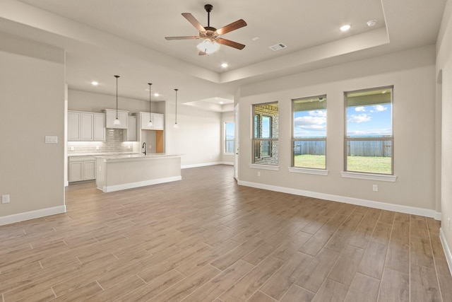 unfurnished living room with sink, a tray ceiling, light hardwood / wood-style flooring, and ceiling fan