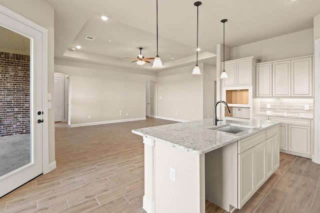 kitchen featuring white cabinetry, sink, a kitchen island with sink, a tray ceiling, and light stone countertops