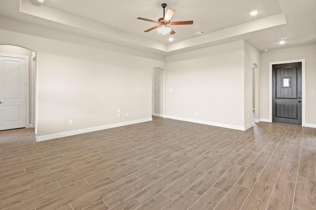 unfurnished living room with ceiling fan, a raised ceiling, and light wood-type flooring