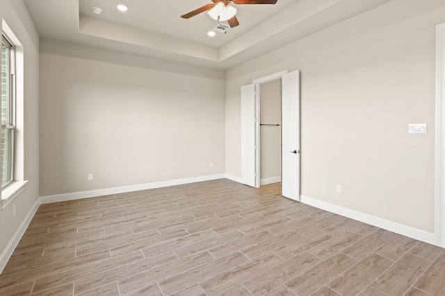 unfurnished room featuring ceiling fan, a tray ceiling, and light hardwood / wood-style floors