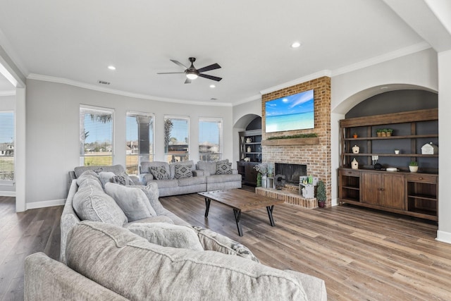 living room with crown molding, a brick fireplace, hardwood / wood-style flooring, and ceiling fan