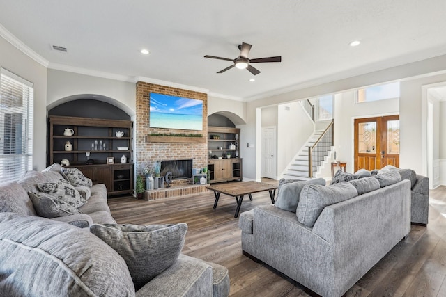 living room featuring built in features, a fireplace, ornamental molding, ceiling fan, and dark wood-type flooring