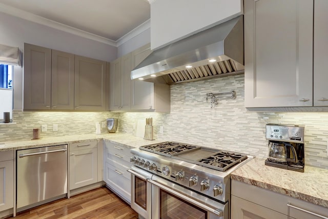 kitchen featuring light stone countertops, wall chimney range hood, stainless steel appliances, and crown molding