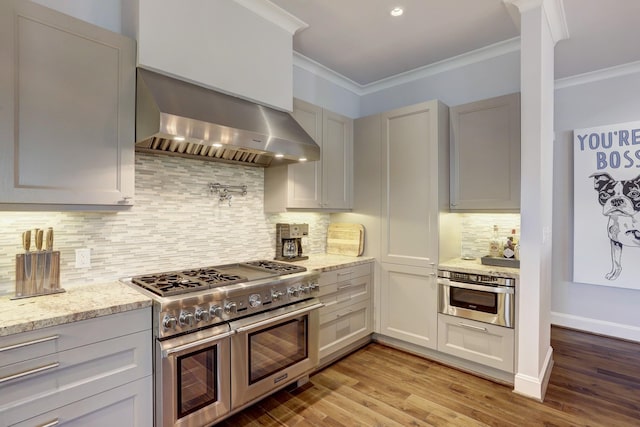 kitchen featuring light wood-style floors, appliances with stainless steel finishes, light stone counters, crown molding, and wall chimney range hood