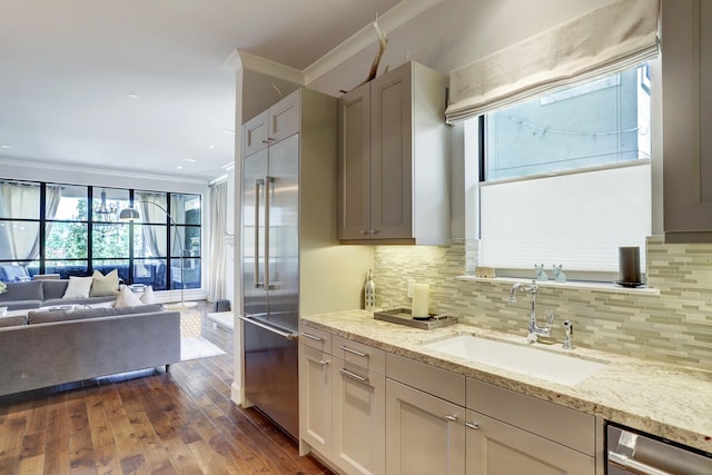 kitchen featuring light stone counters, open floor plan, stainless steel appliances, crown molding, and a sink