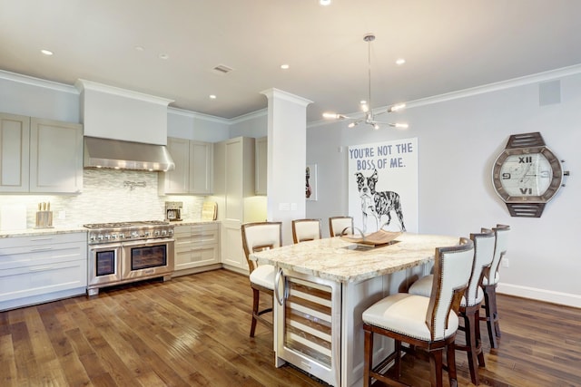 kitchen with a breakfast bar, decorative backsplash, wall chimney range hood, light stone countertops, and double oven range