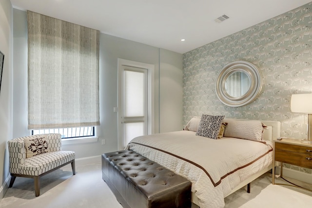 bedroom featuring visible vents, an accent wall, light carpet, baseboards, and wallpapered walls