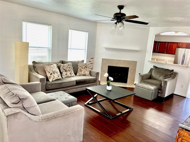 living room with dark hardwood / wood-style flooring, ceiling fan, a tile fireplace, and a textured ceiling