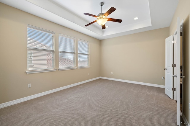 carpeted spare room with a raised ceiling and ceiling fan