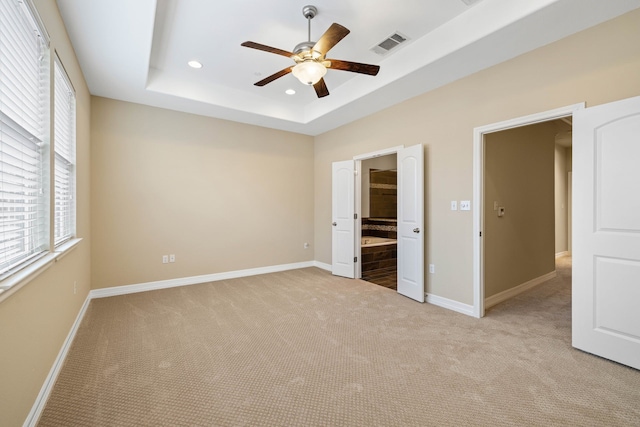 unfurnished bedroom featuring ensuite bathroom, light colored carpet, ceiling fan, and a tray ceiling