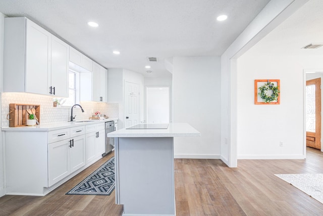 kitchen featuring white cabinets, backsplash, a center island, stainless steel dishwasher, and light wood-type flooring