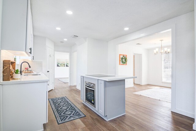 kitchen featuring black electric stovetop, oven, sink, and white cabinets