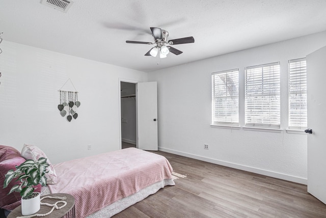 bedroom with ceiling fan, a spacious closet, a textured ceiling, and light wood-type flooring