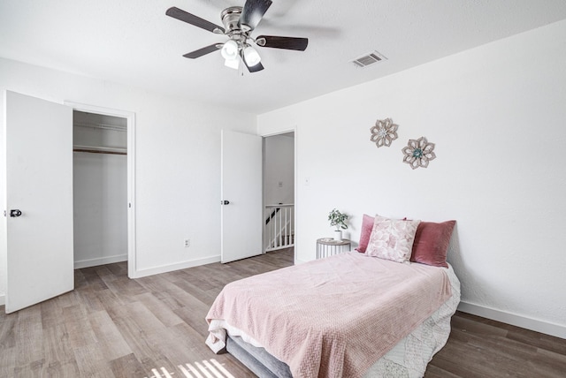 bedroom featuring a walk in closet, visible vents, a ceiling fan, wood finished floors, and baseboards