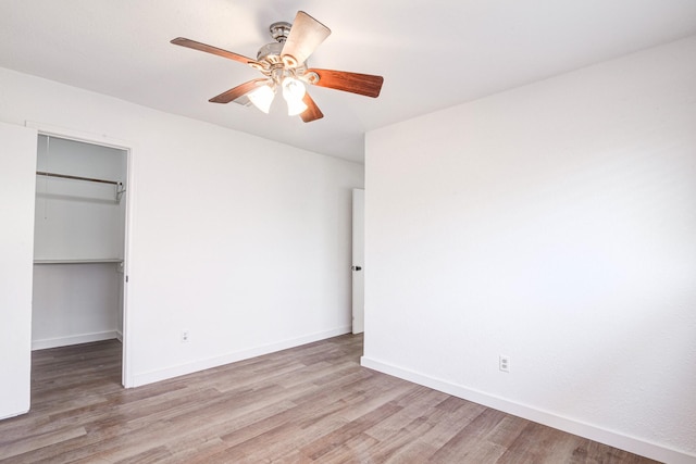 unfurnished bedroom with a walk in closet, a closet, ceiling fan, and light wood-type flooring