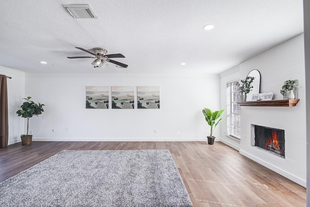 living area with a warm lit fireplace, a textured ceiling, wood finished floors, and visible vents