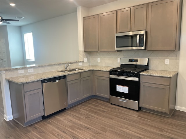 kitchen with sink, tasteful backsplash, appliances with stainless steel finishes, kitchen peninsula, and light stone countertops