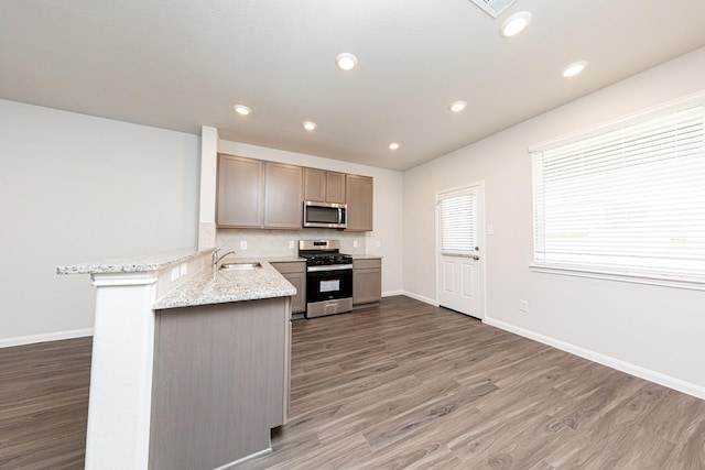 kitchen featuring wood finished floors, a peninsula, a sink, stainless steel appliances, and backsplash