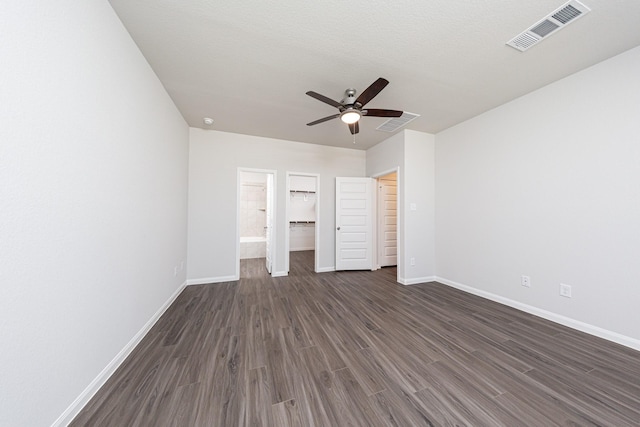 unfurnished bedroom featuring a spacious closet, visible vents, ceiling fan, baseboards, and dark wood-style flooring