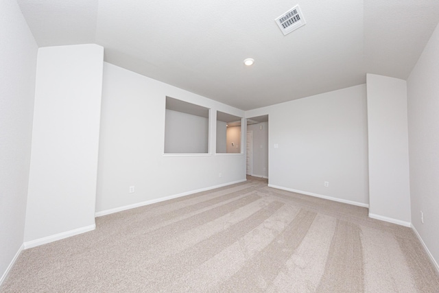 empty room featuring lofted ceiling, baseboards, visible vents, and light carpet