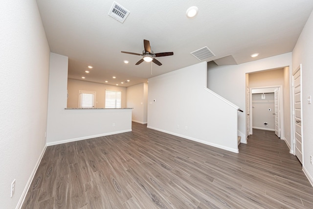 unfurnished living room with visible vents, stairway, ceiling fan, and wood finished floors