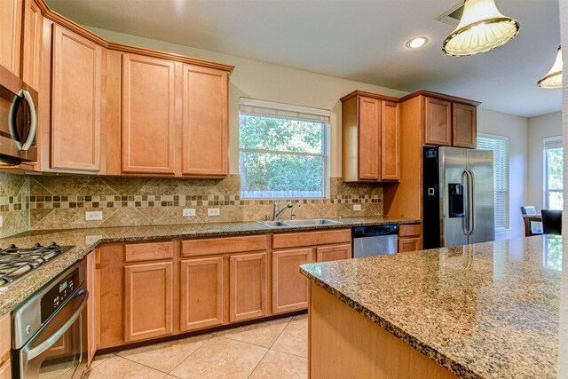 kitchen with sink, light tile patterned floors, backsplash, stainless steel appliances, and decorative light fixtures