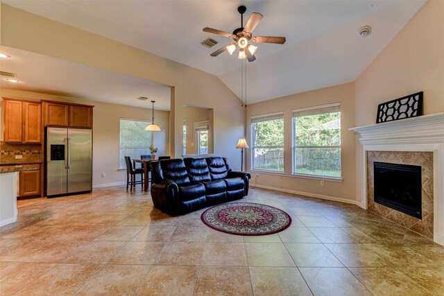 living room featuring ceiling fan, lofted ceiling, a tiled fireplace, and light tile patterned floors