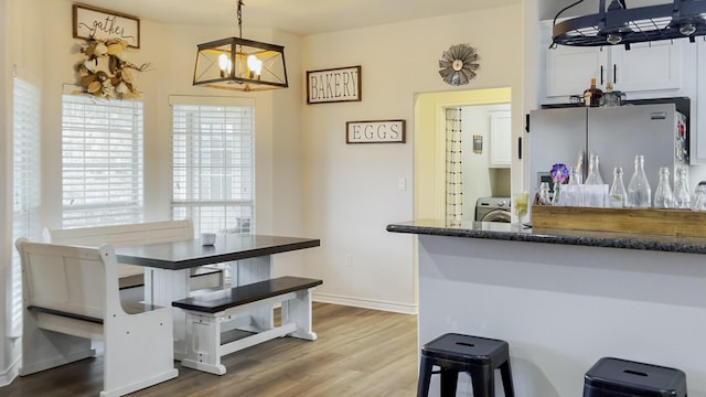 kitchen with a breakfast bar area, white cabinetry, wood-type flooring, decorative light fixtures, and stainless steel refrigerator