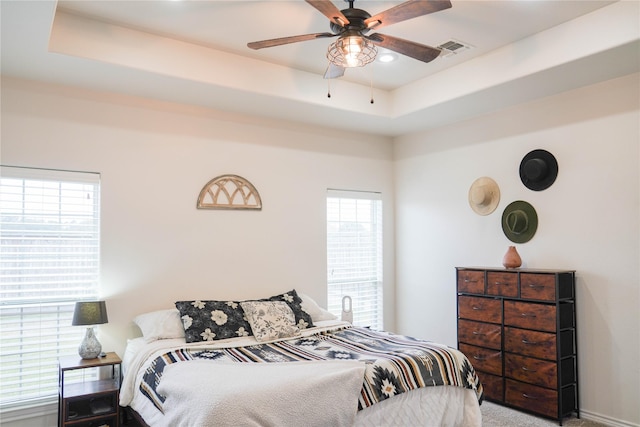 carpeted bedroom with ceiling fan and a tray ceiling