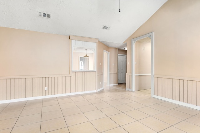 tiled empty room with lofted ceiling and a textured ceiling