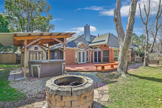 back of property with a deck, a storage unit, a lawn, an outdoor fire pit, and a hot tub