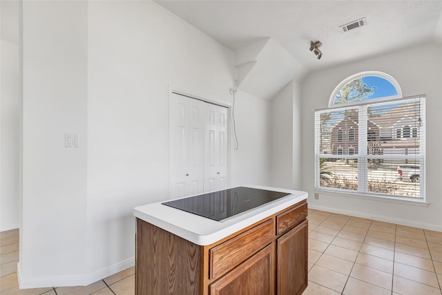 kitchen featuring black electric stovetop, vaulted ceiling, a center island, and light tile patterned flooring