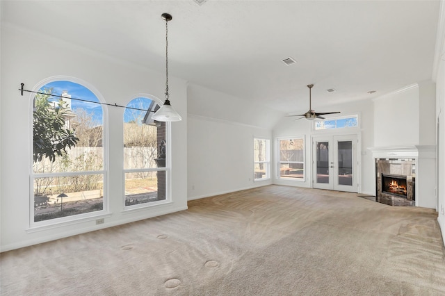 unfurnished living room with french doors, crown molding, ceiling fan, a tiled fireplace, and carpet