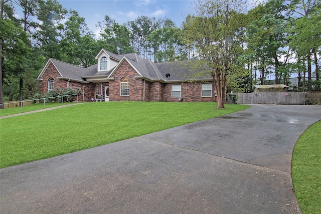 view of front of property with brick siding, roof with shingles, a front yard, fence, and driveway