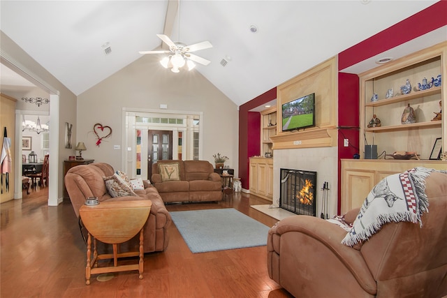 living room with a large fireplace, visible vents, built in features, wood finished floors, and ceiling fan with notable chandelier