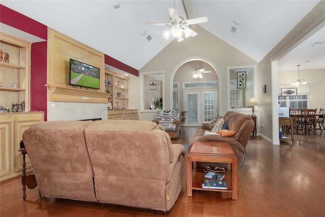 living room with high vaulted ceiling, dark hardwood / wood-style floors, built in features, a tiled fireplace, and ceiling fan with notable chandelier