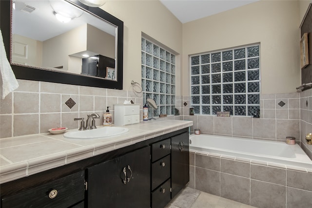 bathroom with tiled bath, visible vents, tasteful backsplash, and vanity