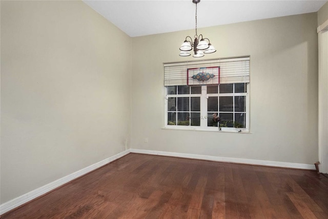 spare room featuring wood finished floors, baseboards, and a chandelier
