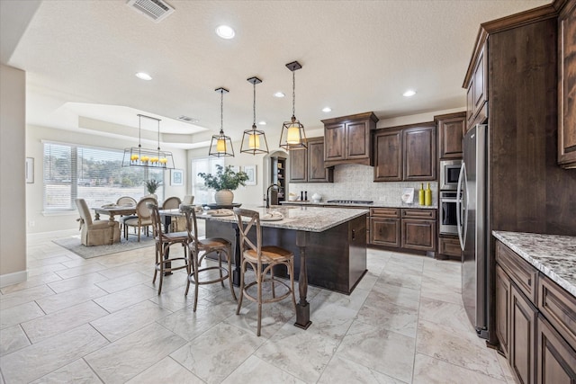 kitchen featuring appliances with stainless steel finishes, decorative light fixtures, an island with sink, a kitchen breakfast bar, and dark brown cabinetry