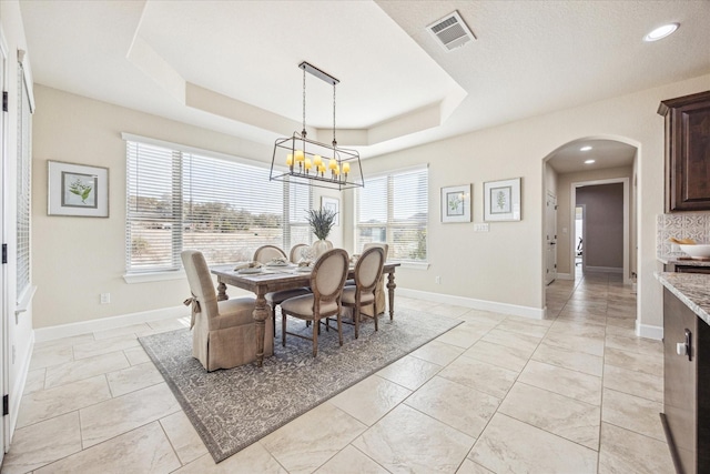 tiled dining space featuring a notable chandelier and a tray ceiling