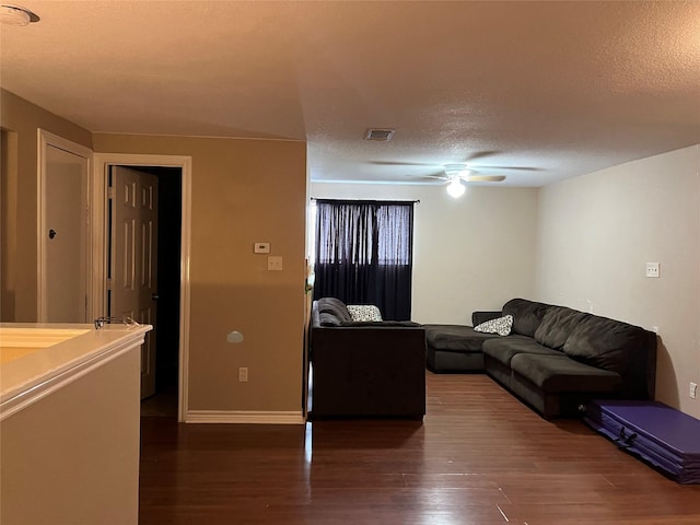 living room featuring dark wood-type flooring, ceiling fan, and a textured ceiling