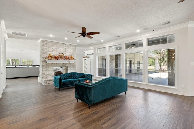 living room featuring crown molding, a textured ceiling, dark hardwood / wood-style floors, ceiling fan, and a fireplace