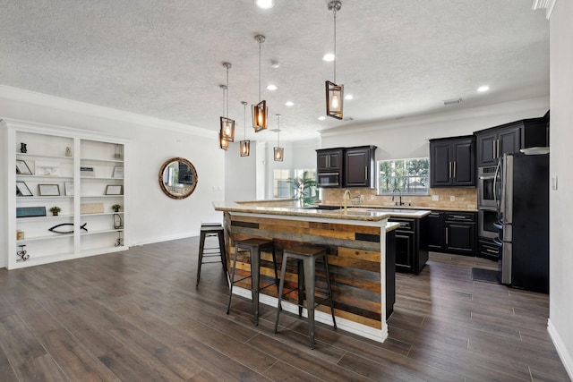 kitchen with pendant lighting, appliances with stainless steel finishes, a kitchen island with sink, a kitchen breakfast bar, and dark hardwood / wood-style flooring