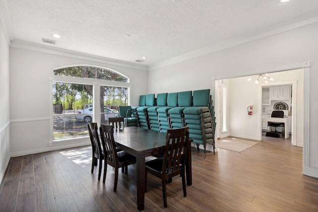 dining area featuring hardwood / wood-style flooring, crown molding, a textured ceiling, and a notable chandelier