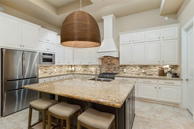 kitchen with backsplash, custom exhaust hood, white cabinets, stainless steel appliances, and a sink