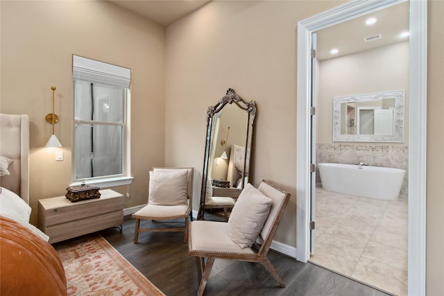 bedroom with visible vents, ensuite bath, baseboards, and wood finished floors